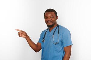 Smiling black surgeon doctor bearded man in blue coat with stethoscope points finger to left photo