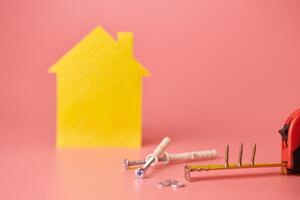 House renovation concept. Home repair and redecorated. Screws and yellow house shaped figure on pink background. photo