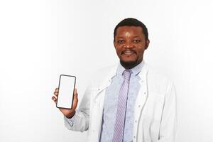 Smiling black doctor man with small beard in white coat holds smartphone blank mockup photo