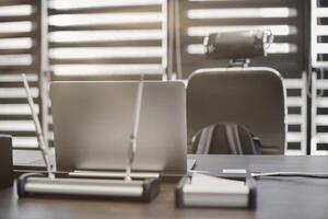 Modern office workplace. Business laptop in work place for chief, boss or other employees. Notebook on work table. Office large corporation. Light through half open blinds photo