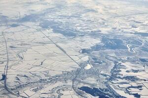 Aerial cloudscape view over clouds top to snow covered rivers, roads, cities and fields, winter air photo