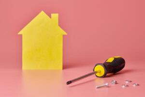 House renovation concept. Home repair and redecorated. Screws and yellow house shaped figure on pink background. photo