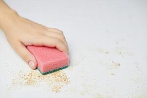 Cleaning kitchen table. Pink sponge in woman hand removes dirt, bread crumbs and leftovers. Household chores photo