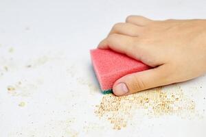 Cleaning kitchen table. Pink sponge in woman hand removes dirt, bread crumbs and leftovers. Household chores photo