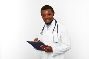 Smiling black bearded doctor man in white robe with stethoscope filling medical records on clipboard photo