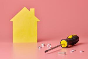 House renovation concept. Home repair and redecorated. Screws and yellow house shaped figure on pink background. photo