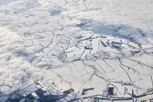 Aerial cloudscape view over clouds top to snow covered rivers, roads, cities and fields, winter air photo