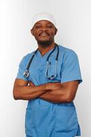 sonriente médico cirujano negro barbudo con abrigo azul y gorra médica con estetoscopio de brazos cruzados foto