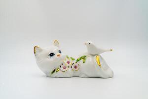 Ceramic statuette, porcelain playful cat. Dove, petals and leaves embellishment, gilded edges. Shiny surface, collectible item. Hand-painted refined. Graceful posture, handcrafted. Black background photo