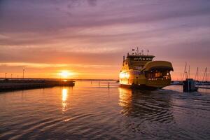 Ferry que sale del puerto a la isla Visingsoe en el lago Vaetten para la puesta de sol. faro foto