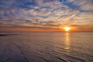 Sunset, illuminated sea. Sandy beach in the foreground. Light waves. Baltic Sea photo