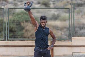 Black muscular athlete lifting kettlebell with one arm photo