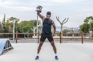 Muscular sportsman exercising with kettlebell in park photo