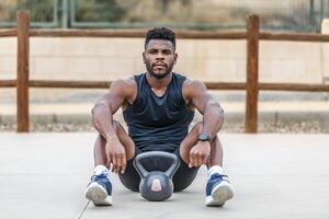 Strong black sportsman resting near kettlebell photo