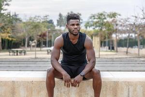 Confident ethnic sportsman resting on border in city photo