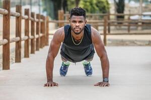 Determined black sportsman doing plank on ground in city park photo