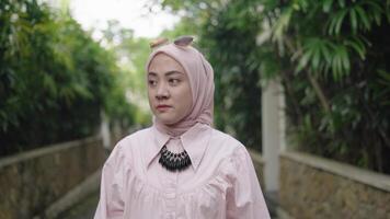 moderno musulmano donna su hijab sud-est asiatico - a passeggio, sorridente, guardare sua smartphone all'aperto video