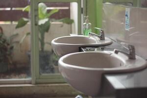 Two washbasin to asia public toilet, Two modern ceramic washbasins, Ceramic sink with chrome mixer in contemporary washroom. photo