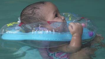 linda pequeño asiático bebé 1 año antiguo niñito niño nadando utilizando azul piscina flotador aprender a nadar lento movimiento video