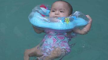 schattig weinig Aziatisch baby 1 jaar oud kleuter kind zwemmen gebruik makend van blauw zwembad drijver leren naar zwemmen langzaam beweging video