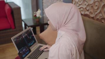 moderno musulmán mujer en hijab Sureste asiático - comercio invertir en valores mercado cripto forex mediante su ordenador portátil mostrando gráfico gráfico video