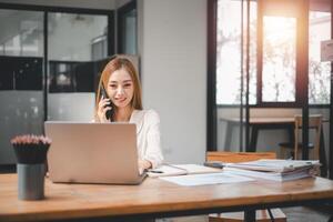 Young busy Asian business woman executive working on laptop making call in creative office, Professional businesswoman manager talking to client using computer, Business concept. photo