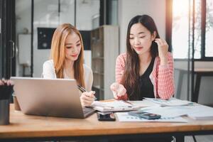 contento multiétnico sonriente negocio mujer trabajando juntos en oficina, utilizando calculadora y ordenador portátil computadora a calcular financiero informe. foto