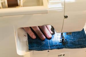 hombre utilizando un de coser máquina con un azul prenda, para reparar trabajar, personalización, creación, reciclado foto