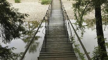 Wooden bridge suspended over forest river. Stock footage. Old hanging wooden bridge over which travelers are afraid to cross photo