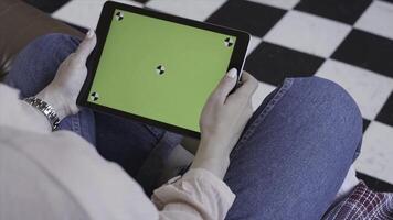 Young woman using black tablet device with green screen. Stock footage. Woman holding tablet, zooming pages while sitting on the couch in the living room. Chroma key. photo