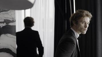 Young caucasian man dressed in formal classic clothes looking pensive. Action. A man in suit standing in front of mirror in the room. photo