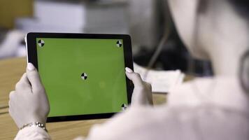 Rear view of a brunette woman using tablet with green screen, modern technologies concept. Stock footage. Female holding ipad with chromakey and reading something. photo