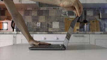 Concept of working at home during isolation. Action. Side view of male hands openning new silver laptop that is standing on the white table in the kitchen. photo