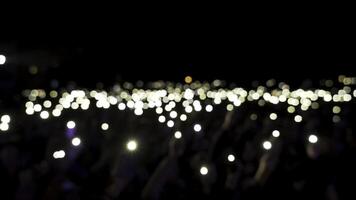 desenfocado público en salón con luces ondulación en el oscuro. acción. audiencia participación Los telefonos con brillante linternas durante el concierto, romántico atmósfera. foto