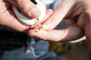 Woman pricking her finger to check blood glucose level with glucometer, test blood glucose for diabetes photo