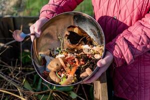 Person who put in a composter some kitchen waste like vegetables, fruits, eggshell, coffee grounds in order to sort and make bio fertilizer photo