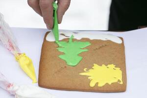 Hand draws Christmas tree on gingerbread with cream icing. photo