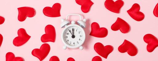 hora para amor. alarma reloj y rojo corazones en un rosado antecedentes. San Valentín día concepto, bandera formato. foto