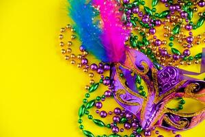 Carnival mask and beads on yellow background. Mardi Gras concept. Fat Tuesday symbol. photo