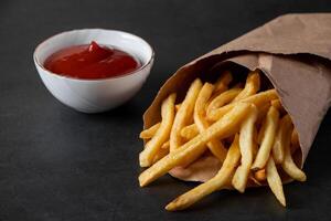 Hot crispy fries in a paper bag on black background. Tasty american fast food. photo