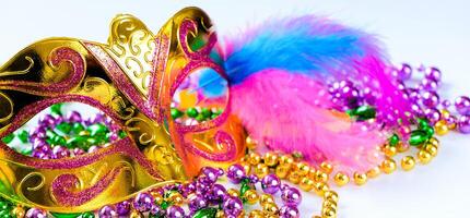 Golden carnival mask and colorful beads on white background. Closeup symbol of Mardi Gras or Fat Tuesday. photo