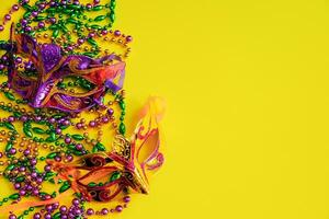 Two multi-colored carnival masks and beads on yellow background. Mardi Gras concept. Fat Tuesday symbol. photo