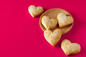 azúcar galletas corazones en un de madera plato en rosado antecedentes para San Valentín día. foto