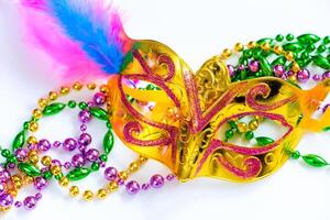 Golden carnival mask and colorful beads on white background. Closeup symbol of Mardi Gras or Fat Tuesday. photo