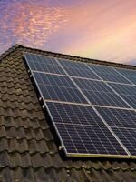 Solar panels producing clean energy on a roof of a residential house with a sunset sky. photo