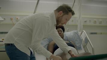 jovem africano mulher com encaracolado cabelo deitado dentro clínica cama falando para médico video