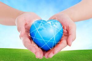 Female hands holding on earth global heart on grassland. photo