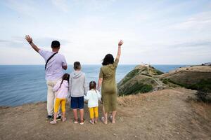 Happy family of five tanding on top of a mountain and looking at the sea and hands up. Cape Emine, Black sea coast, Bulgaria. photo