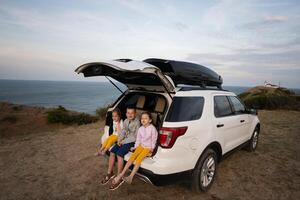 Three kids sitting in the trunk of a car on the beach at sunset. Cape Emine, Black sea coast, Bulgaria. photo
