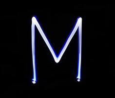 M Mike alphabet hand writing blue light  over black background. photo